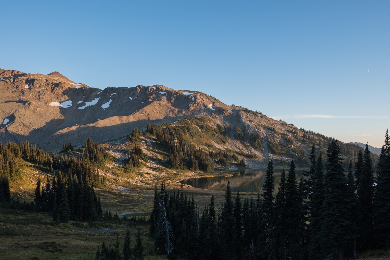 Warm evening light on a mountain ridge, alpine lake, and evergreen forest in Garibaldi Provincial Park.